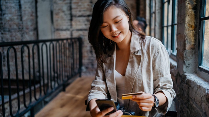 Young woman sits at a cafe smiling with credit card and smartphone in hand
