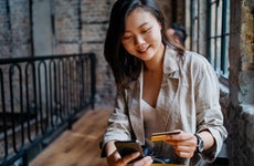 Young woman sits at a cafe smiling with credit card and smartphone in hand