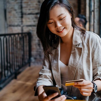 Young woman sits at a cafe smiling with credit card and smartphone in hand