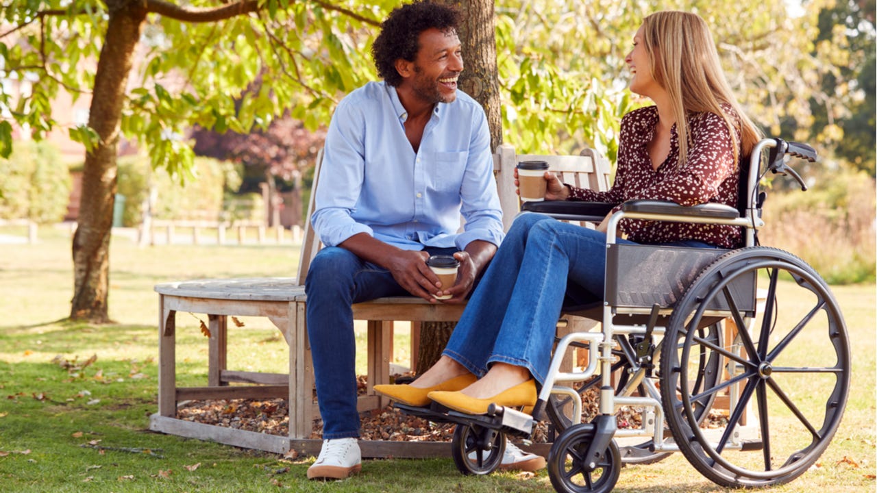 Woman in wheelchair talks with man sitting on a bench
