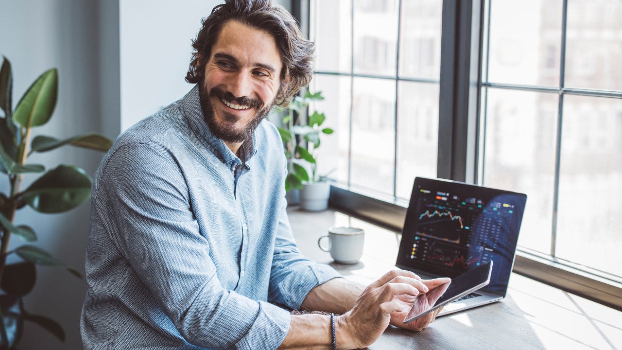 Man at home looking at investments on laptop and phone