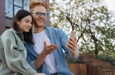 Young man shows young woman something on his smartphone screen outdoors