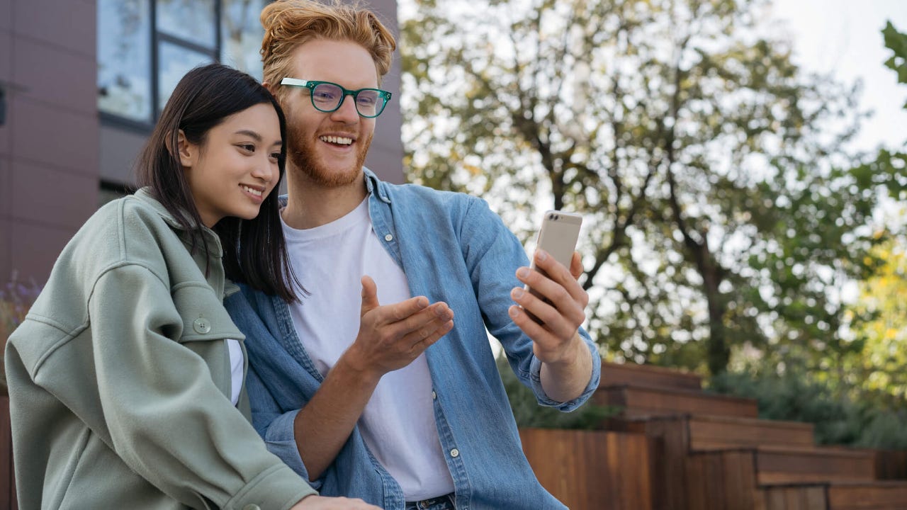 Young man shows young woman something on his smartphone screen outdoors