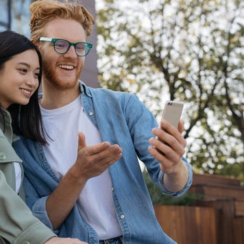 Young man shows young woman something on his smartphone screen outdoors