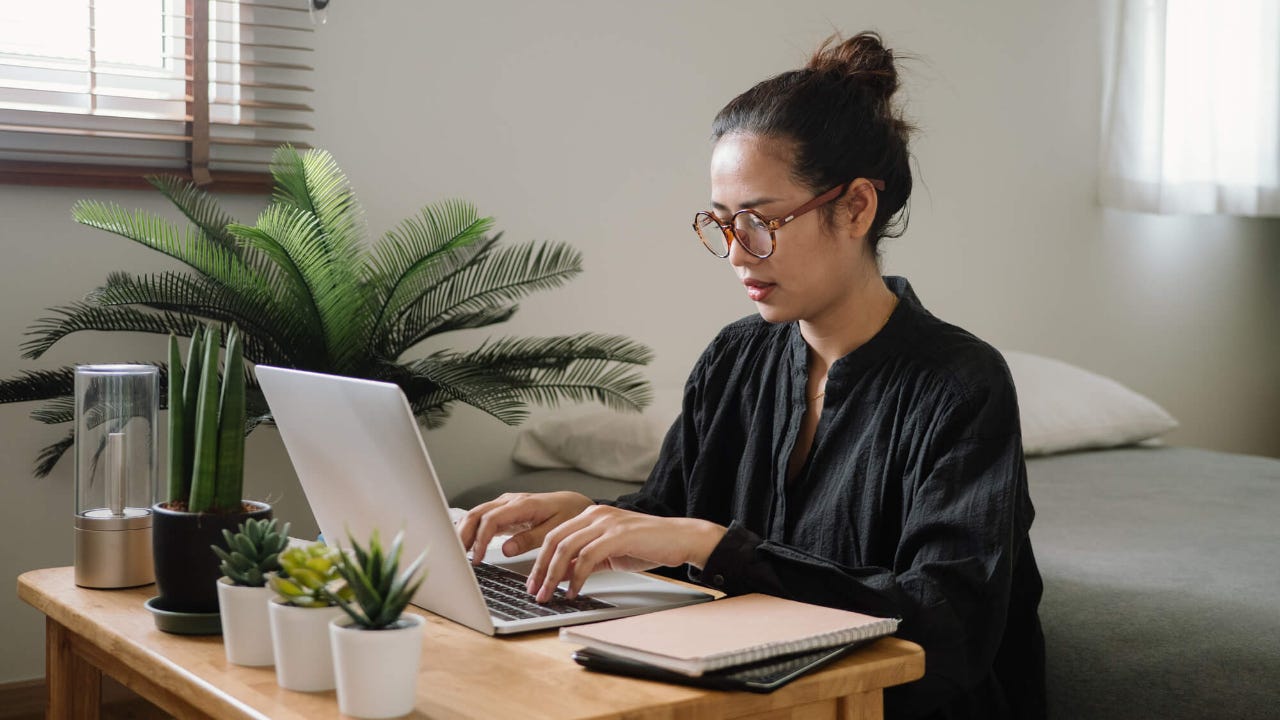 Young woman with glasses sits at home desk with laptop