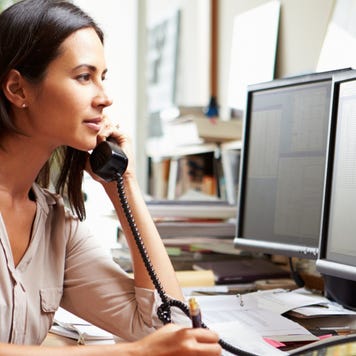 Woman speaks on the phone while looking at computer monitors