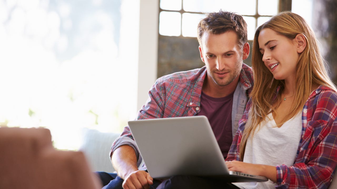 A couple looks at a laptop at home on their couch