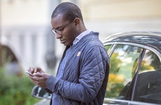 Young man leaning against car using cell phone