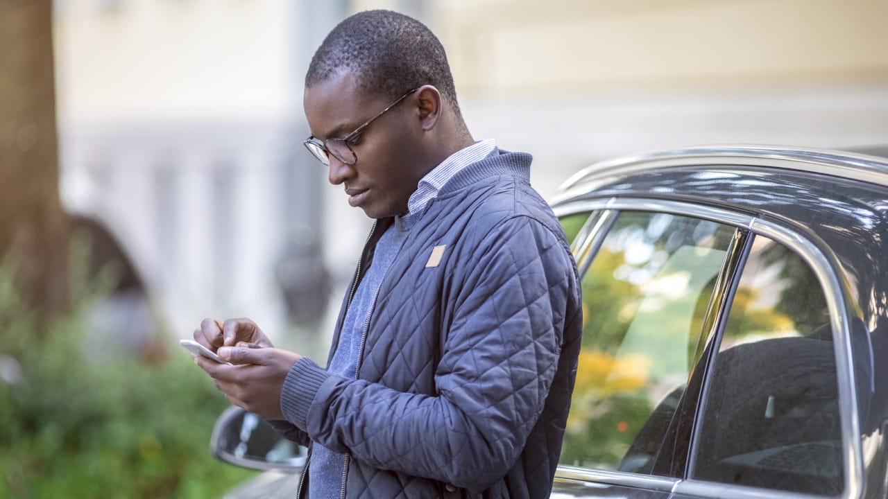 Young man leaning against car using cell phone