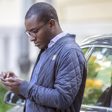 Young man leaning against car using cell phone