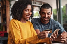 Young woman uses smartphone and smiles with credit card in hand with a young man