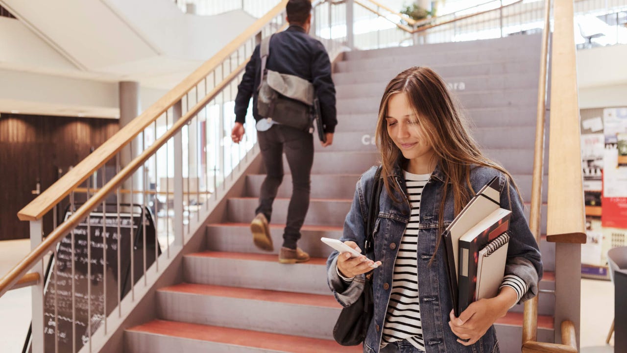 Female student using mobile phone while man walking up on steps in university