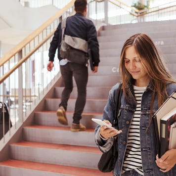 Female student using mobile phone while man walking up on steps in university
