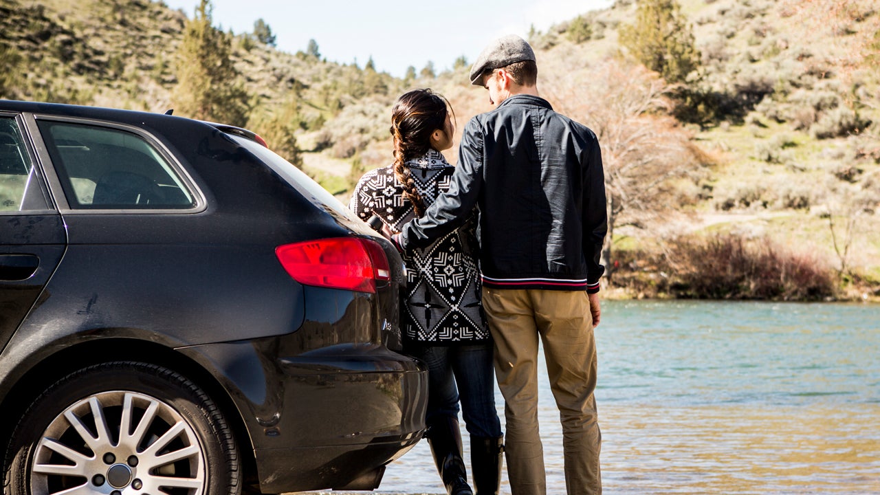 couple standing next to car and looking at lake car