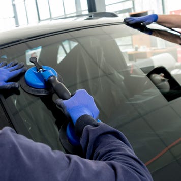 Automobile special workers replacing windscreen or windshield of a car in auto service station garage.