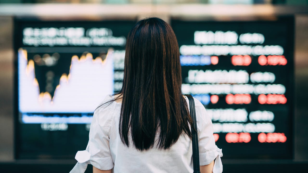 Rear view of businesswoman looking at stock exchange market display screen board in downtown financial district