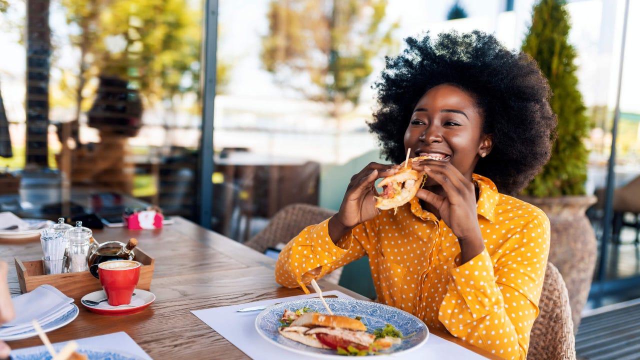 Smiling young woman takes a bite of a sandwich at a restaurant