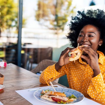 Smiling young woman takes a bite of a sandwich at a restaurant