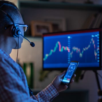 A man looks at his phone and computer screen while trading