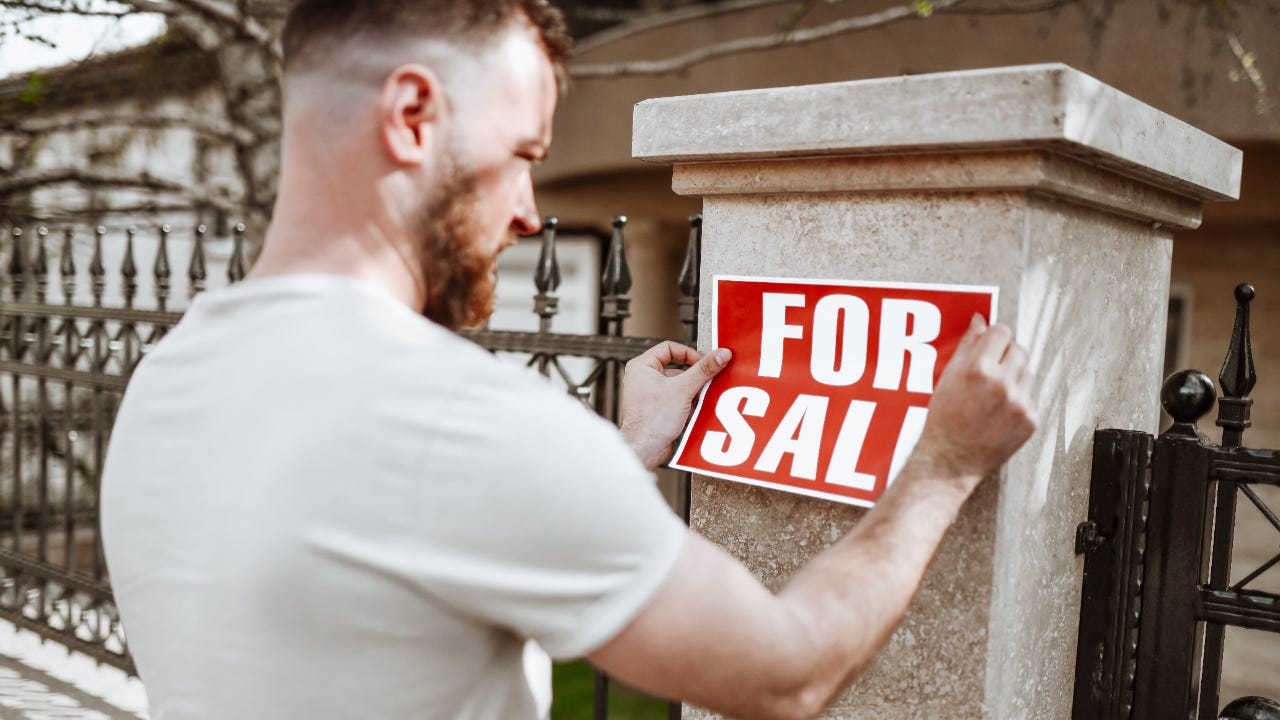 Bearded Male Sticking For Sale Sign On House Yard Post