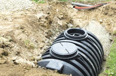 A black septic tank halfway buried in dirt outside