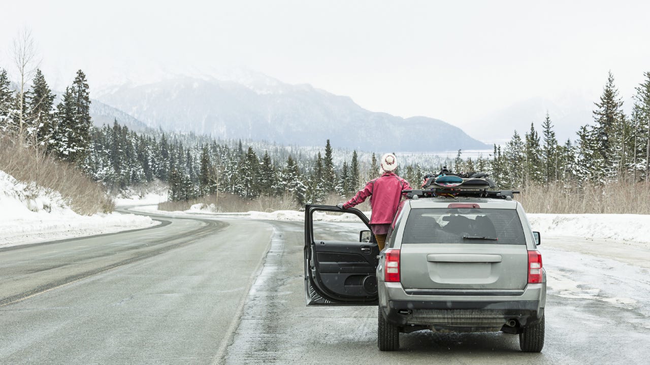 Caucasian woman standing in car in winter admiring scenic view