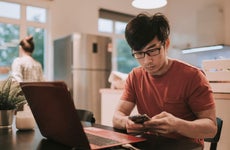 Young man works at kitchen table with laptop and smartphone