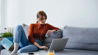Young woman sits on her couch at home with her laptop and credit card in hand