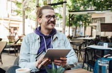 Young man at outdoor cafe smiles as he holds his tablet and credit card