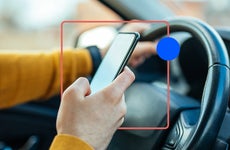 Close-up of a hand holding a smartphone while the driver is presumably driving.