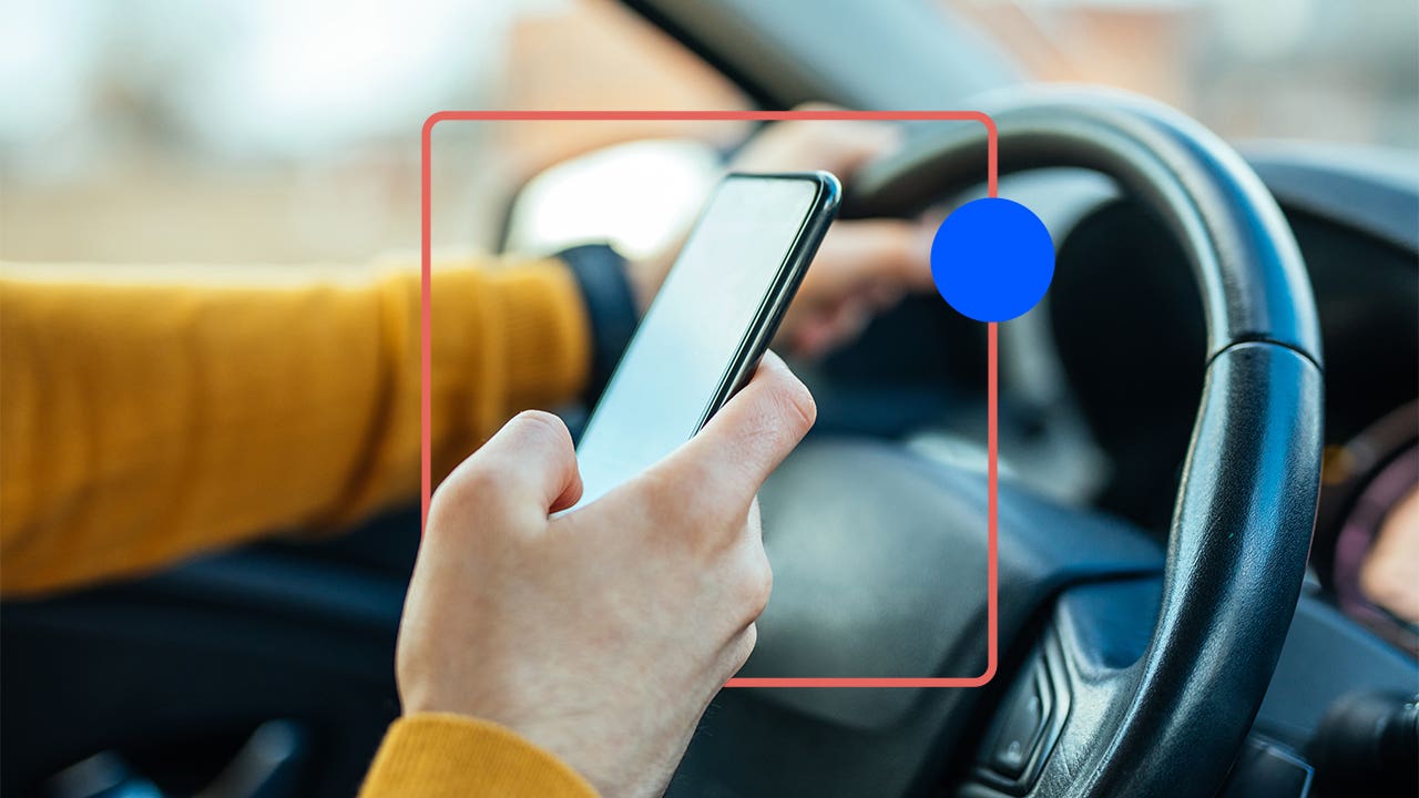 Close-up of a hand holding a smartphone while the driver is presumably driving.