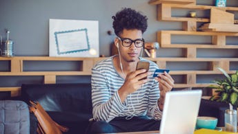 Young man working from home on the couch with credit card in hand