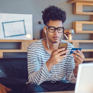 Young man working from home on the couch with credit card in hand