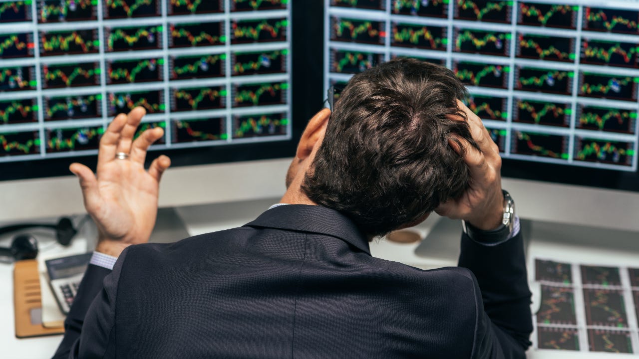 A trader sits frustrated in front of his computer monitors