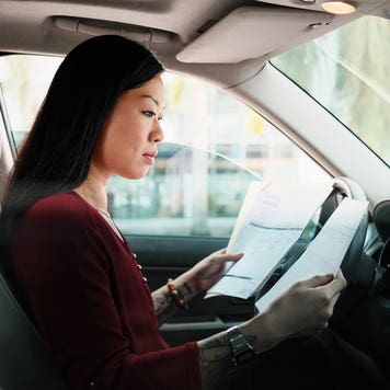 Driver sitting in their car with the window down, reviewing documents. The car is not in motion.