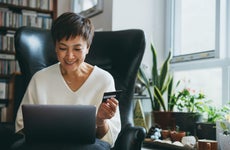 Smiling senior woman holds her credit card and uses her laptop in her home office