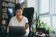 Smiling senior woman holds her credit card and uses her laptop in her home office