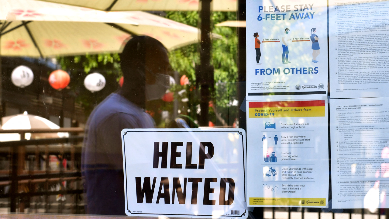 A 'Help Wanted' sign is posted beside Coronavirus safety guidelines in front of a restaurant.