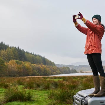 Young traveler standing on her car hood takes a photo of the forest landscape around her
