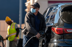 A person wearing a protective mask holds a fuel pump nozzle at a Chevron Corp. gas station in San Francisco, California.