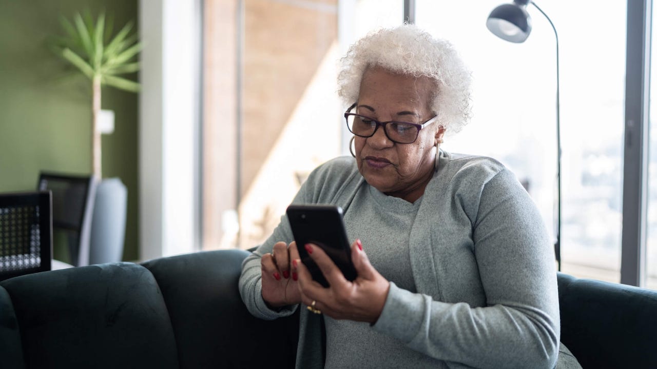 Senior woman using smartphone sitting on the couch at home