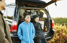 Smiling sisters hanging out at back of car after finishing backpacking trip