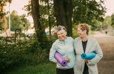 Two senior women with yoga mats walk in the park