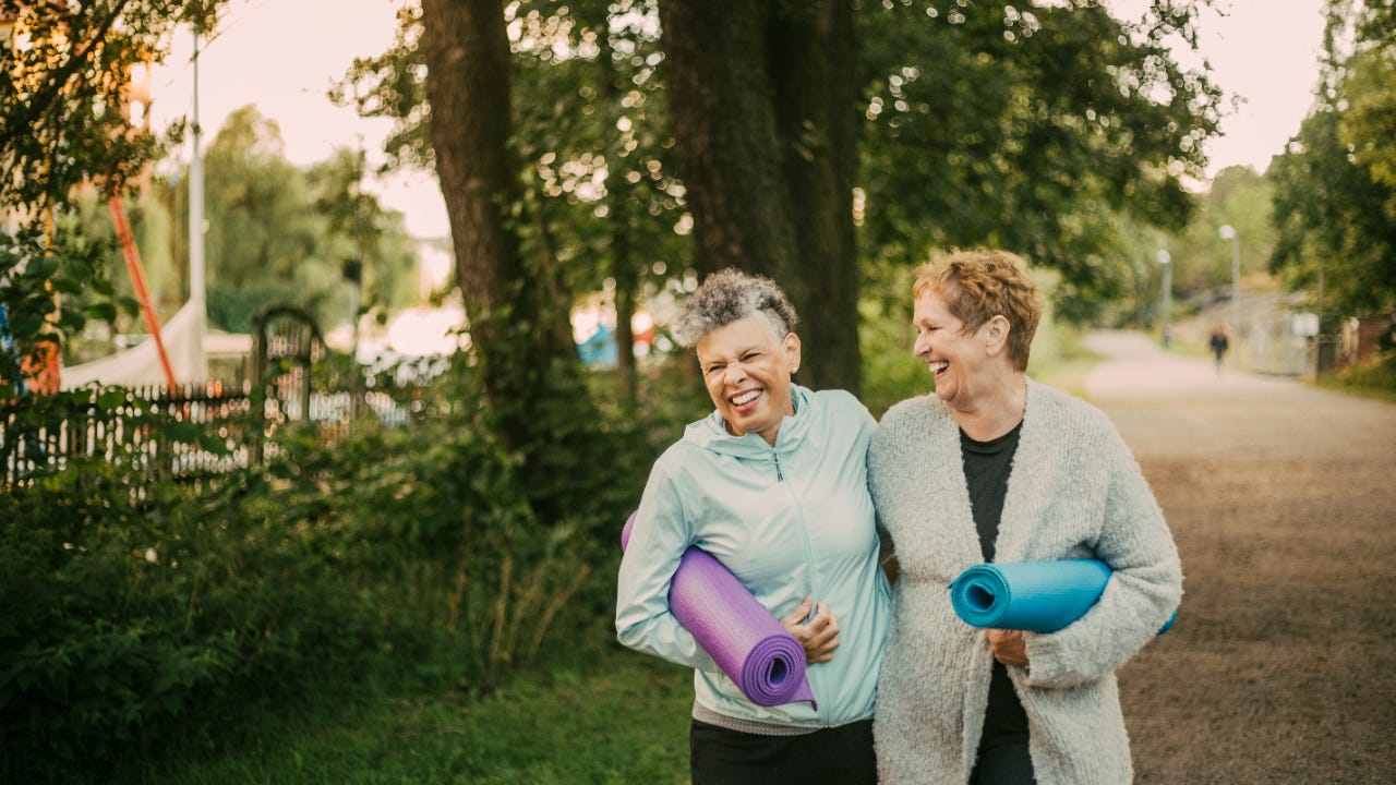 Two senior women with yoga mats walk in the park