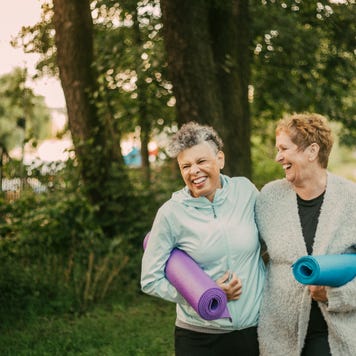 Two senior women with yoga mats walk in the park