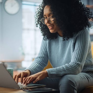 Young woman in her living room smiling and using her laptop