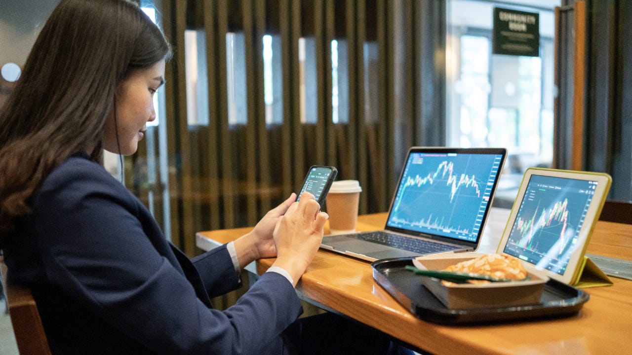 A woman trades on her phone and laptop