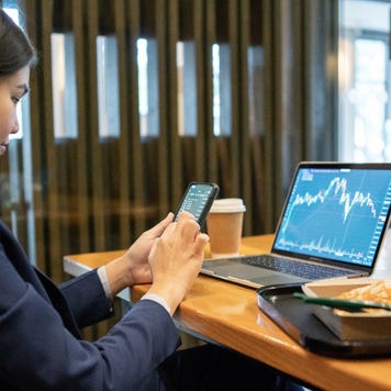 A woman trades on her phone and laptop