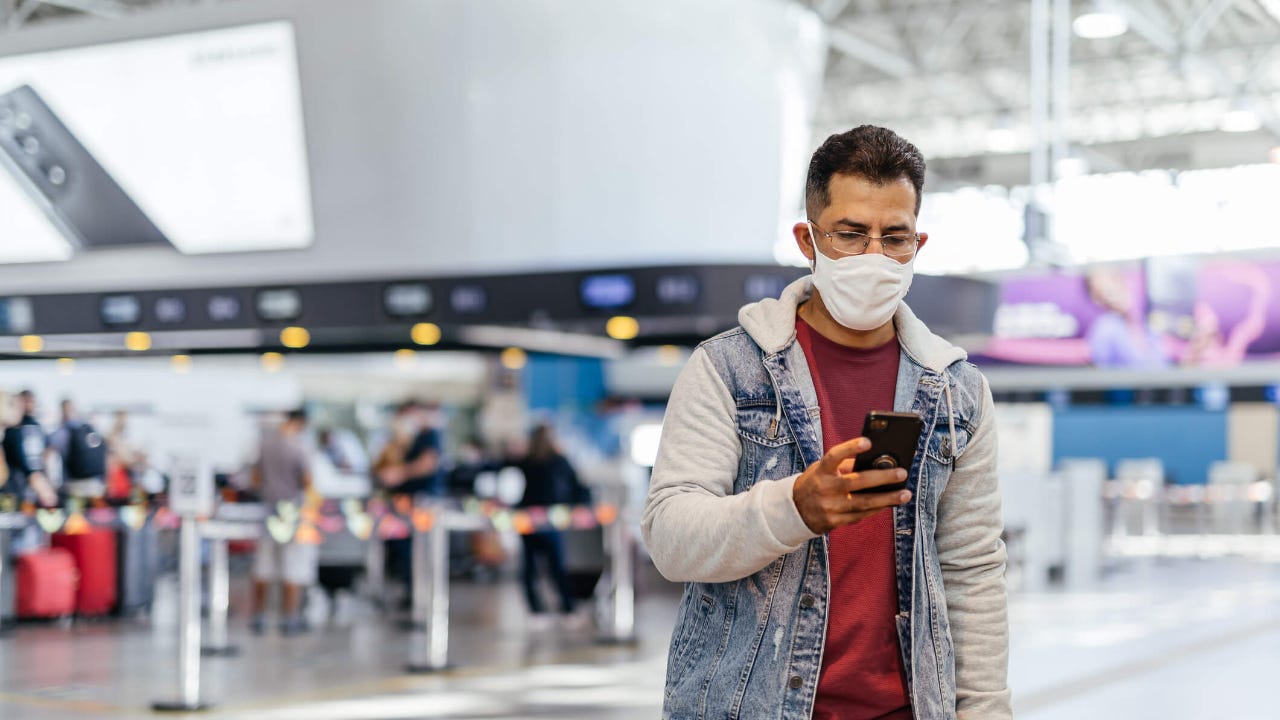 Adult man uses his smartphone in an airport terminal with a mask on