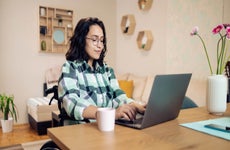 Young woman in a wheelchair uses her laptop in her bedroom at a desk